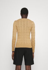 Vaalea beige nyöritetty neulepaita, jossa on slim fit -leikkaus, pyöreä pääntie sekä ribbireunat hihoissa ja helmoissa. Yhdistetty mustien shortsien kanssa.