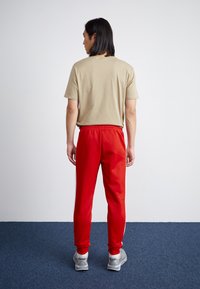 Beige bomull t-skjorte, røde joggebukser med elastisk midje, med sidelister, paret med grå sneakers. Synlig flat teppeoverflate.