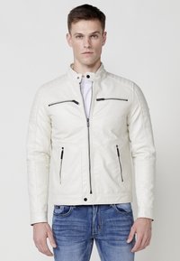 Chaqueta de moto de cuero sintético blanco con un alto cuello, bolsillos con cremallera, acentos acolchados en los hombros y un diseño ajustado.
