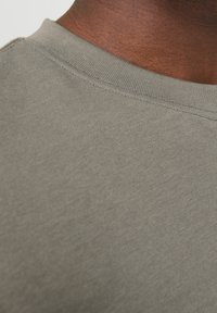 Lys grå T-shirt, tæt på, der fremhæver den glatte tekstur, ribbet rund hals og subtile syninger.