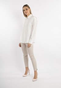 Camicia bianca con bottoni e maniche lunghe, abbinata a pantaloni attillati beige chiaro e scarpe col tacco alte color rosa pallido. Design semplice e pulito.