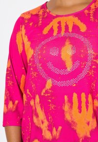 Rosa und orange Batik-T-Shirt mit Dreiviertelärmeln, das ein Strasslächelgesicht-Design auf der Vorderseite zeigt. Aus weichem Baumwollmaterial.