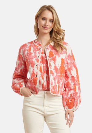 Quilted jacket in coral and white with a floral pattern, features a round neckline, snap buttons, and puffed sleeves. Paired with a light top.