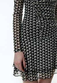 Zwarte en beige patroon jurk met lange transparante mouwen en een gerimpeld zijdetail, met een gelaagde, uitlopende zoom.