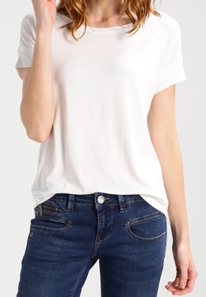 T-shirt blanche à manches courtes avec une coupe décontractée, associée à un jean skinny bleu foncé comprenant des poches avant et des détails de surpiqûres subtils.