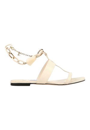 Beige flat sandal with two thin straps, a wide midfoot strap, and a decorative ankle chain with a small charm.