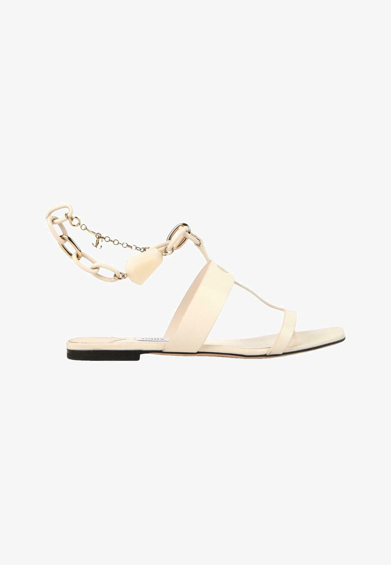 Sandale plate beige avec deux fines brides, une bride large au milieu du pied et une chaîne décorative à la cheville avec un petit charme.