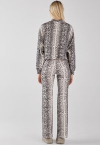 Skórzany płaszcz w wzór węża i dopasowane spodnie w kształcie dzwonów w odcieniach szarości i beżu, charakteryzujące się gładką teksturą i dopasowanym krojem.