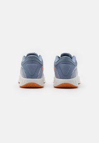 Blå atletiske sko med teksturerede mesh-overlayer, polstret krave og orange detaljer. Holdbar hvid sål med en segmenteret brun ydersål.