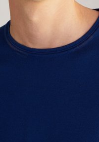 Gros plan sur le cou et la partie supérieure de la poitrine d'une personne portant un pull en maille bleu marine à col rond.