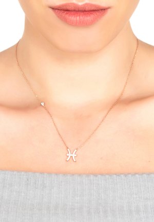 Rose gold necklace with a Pisces symbol pendant, featuring small clear gemstones, on a delicate chain, worn close to the collarbone.