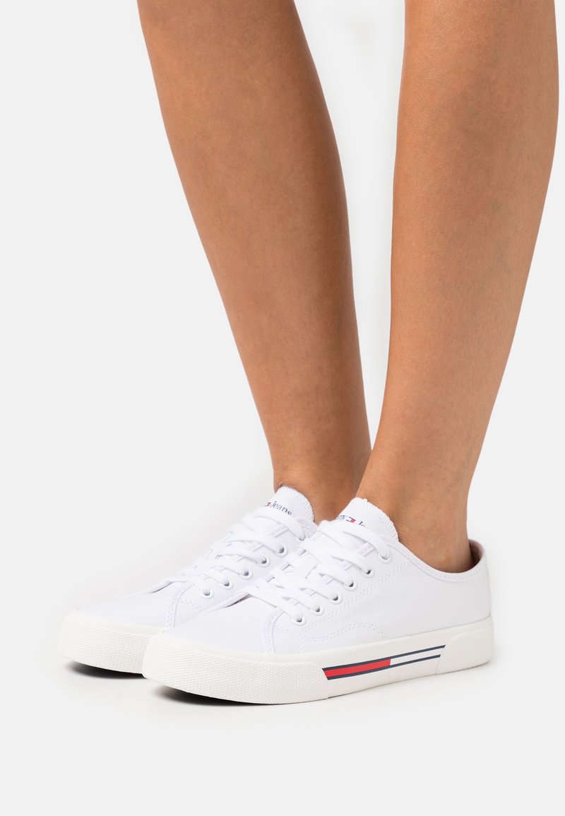 Sneakers bianchi in tela con chiusura a lacci, punta rotonda e suola in gomma. Presentano sottili strisce rosse e blu sul pannello laterale.
