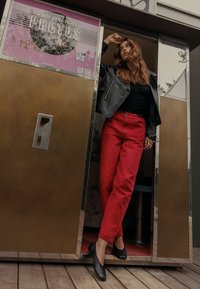 Must musta nahkjakkk, must kitsa ülemineku, punased sirged püksid ja mustad lamejalatsid. Pilt näitab fotonurga, millel on metallist viimistlus.