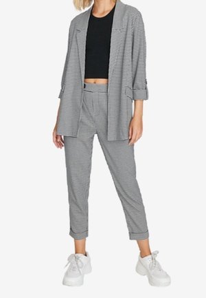 Blazer a righe bianche e nere e top corto abbinato a pantaloni cropped dello stesso colore e sneakers bianche. Il blazer presenta un colletto a punte.
