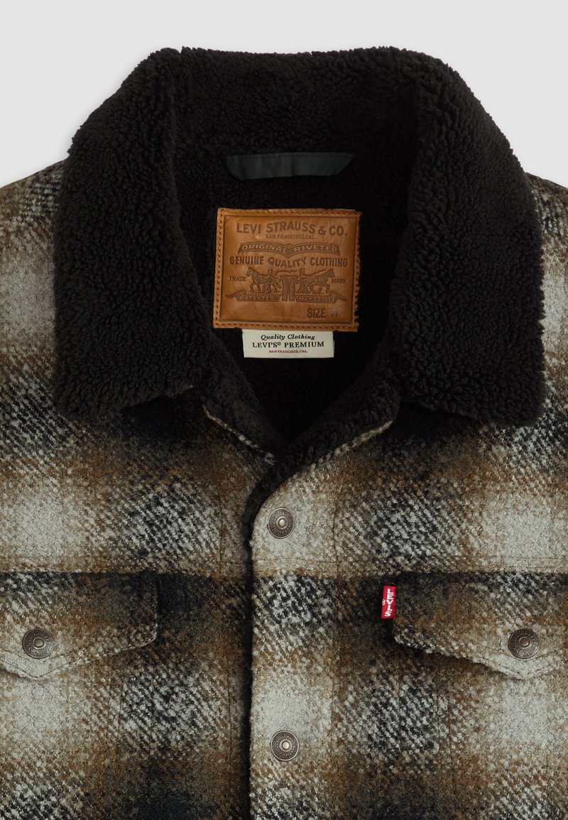 Camicia di flanella a quadri marrone e nera con colletto in shearling, chiusure con bottoni, tasche frontali e un'etichetta in pelle con il marchio Levi's.