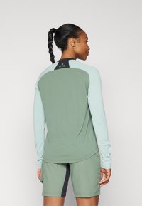 Longermet sportslig topp i mintgrønn med et mørkegrønt panel bak, kombinert med grå shorts med sidelomme.