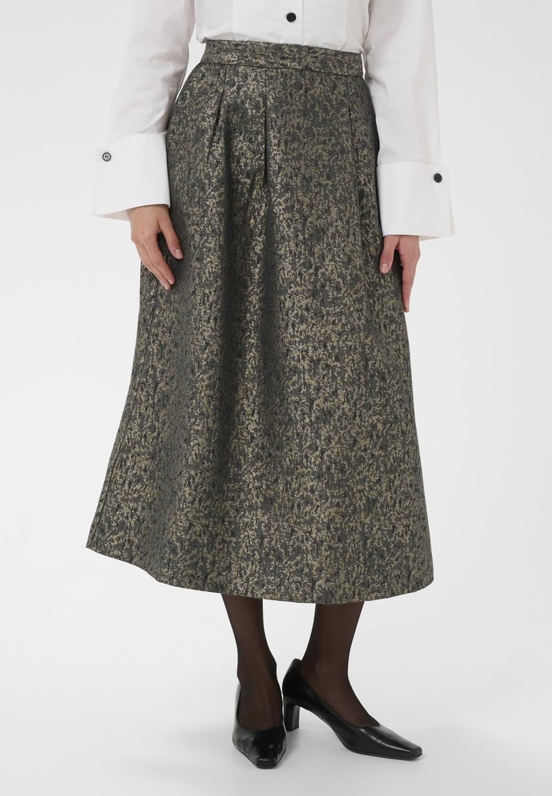 Ilgas, plisuotas sijonas struktūrizuoto tamsiai pilko atspalvio su auksiniais akcentais. Dėvimas su baltu marškinėliu, juodomis pėdkelnėmis ir juodais aukštakulniais batais.