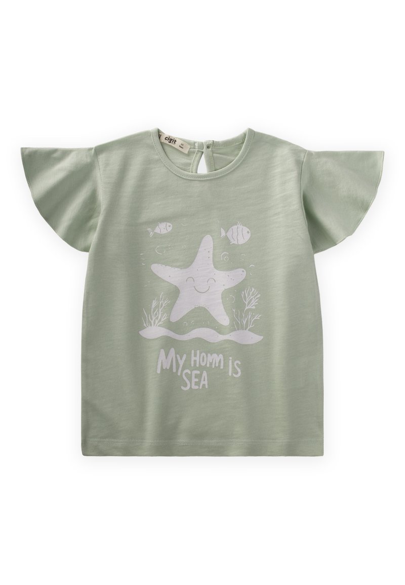 Gaiši zaļš T-krekls ar īsām plandošām piedurknēm, ar baltu zvaigžņu zivtiņu grafiku un tekstu "Mans mājoklis ir jūra" zemāk. Mīksta auduma tekstūra.