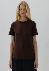 Brązowa koszulka z krótkim rękawem z miękkiej bawełny, z okrągłym dekoltem i luźnym krojem, w zestawieniu z ciemnoniebieskimi spodniami.