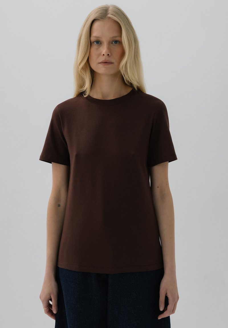 Brązowa koszulka z krótkim rękawem z miękkiej bawełny, z okrągłym dekoltem i luźnym krojem, w zestawieniu z ciemnoniebieskimi spodniami.