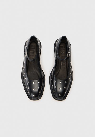 Sapatos de pele preta com bico quadrado, adornados com detalhes em tachas prateadas e uma tira com fivela. Textura suave com um acabamento mate.