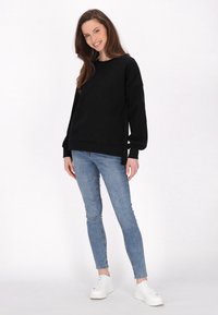 Felpa nera con maniche lunghe e polsini a costine, abbinata a jeans skinny azzurri chiari e sneakers bianche. Tessuto liscio, vestibilità casual.