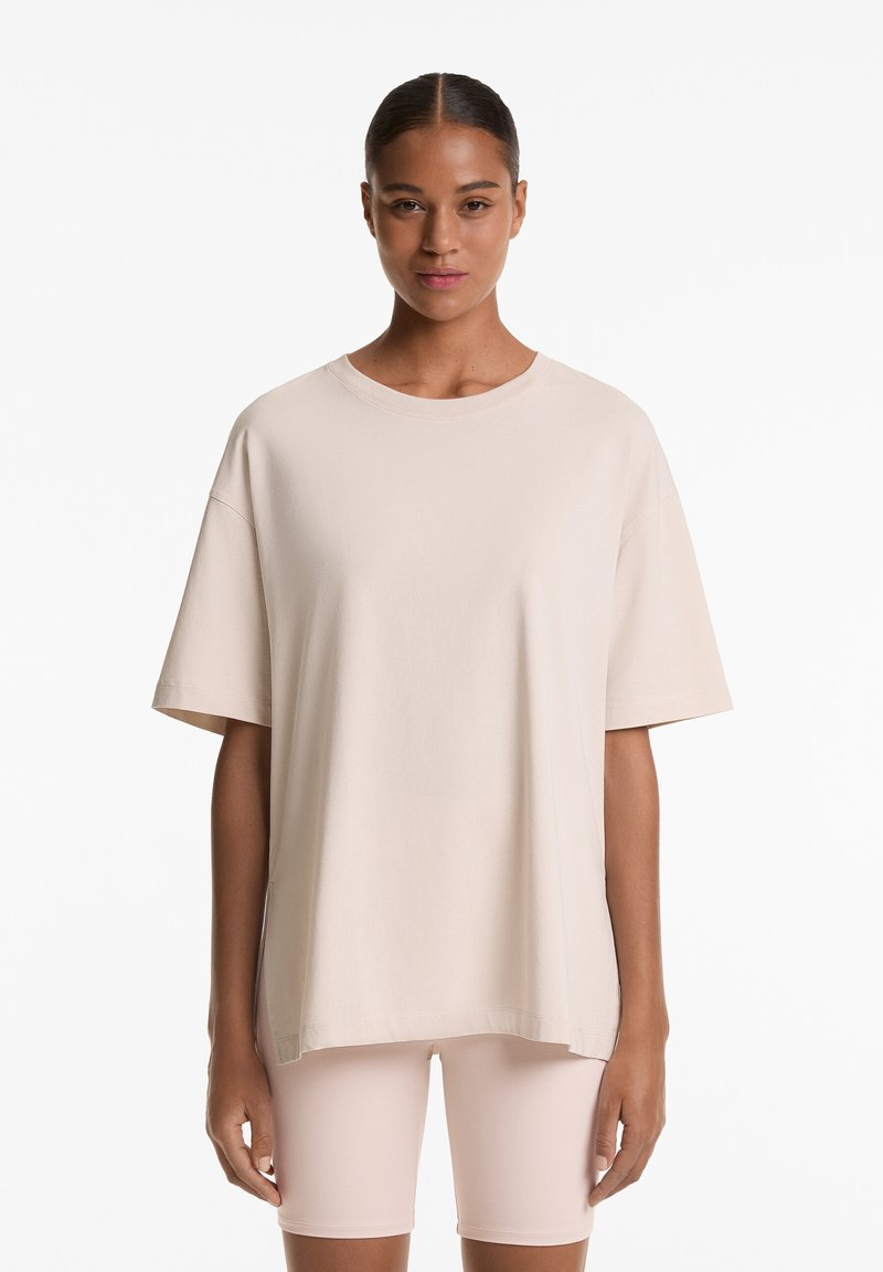 Light beige oversized t-shirt made of cotton with short sleeves, round neckline, and a relaxed fit, paired with light pink shorts.