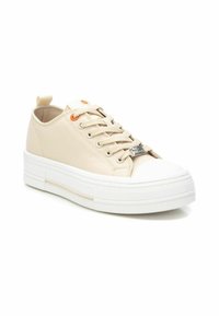 Zapatilla de lona beige con suela de goma blanca, puntera redonda y un ojal naranja en contraste. Presenta cordones y una lengüeta en la parte posterior.