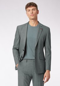 Lichtgrijze colbert en broek met een gestructureerd gebreid blauw overhemd. Het colbert heeft een notch-lapel en een sluiting met één knoop.