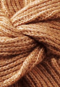 Tissu tricoté de couleur beige chaud, présentant un tissage épais et texturé avec des motifs entrelacés, mettant en valeur des détails de fil doux et duveteux.