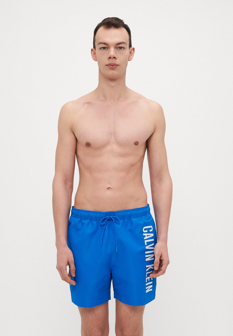 Blaue Badehose mit elastischem Bund und Kordelzug. Mit einem weißen "CALVIN KLEIN" Logo auf der Seite. Weicher Stoff.