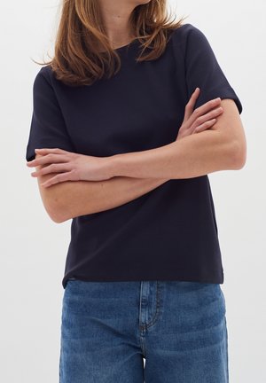 Marineblå kortærmet top lavet af glat stof med rund halsudskæring og en afslappet pasform, kombineret med lyseblå denimjeans.