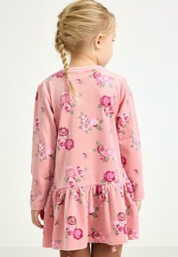Pink fleece dress with long sleeves, featuring a floral pattern in darker pink and green. The design includes a ruffled hem.