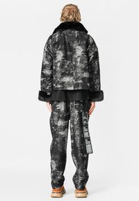 Chaqueta forrada de piel con un patrón en negro y gris, junto con pantalones a juego. Presenta un diseño corto, una textura suave y un detalle de etiqueta colgante.