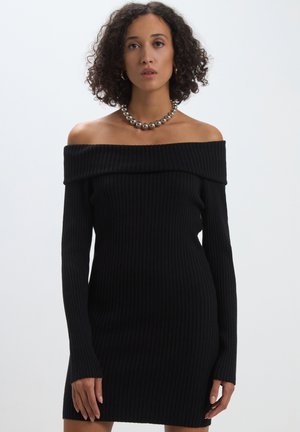 Abito nero a coste con scollo off-the-shoulder e maniche lunghe. Silhouette aderente e texture morbida, design minimalista.