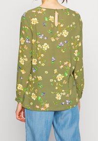 Zielona oliwkowa bluzka z długim rękawem, zdobiona kwiatowym wzorem w żółtym i niebieskim kolorze, z detalem kluczykowym i guzikiem z tyłu. Miękka tekstura materiału.