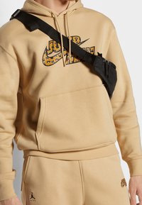 Sudadera con capucha beige con un gran logo de Nike multicolor; combinación con pantalones a juego. Bolso cruzado negro que aporta contraste y funcionalidad.