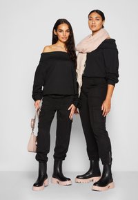 Dva modela nose off-shoulder crne majice i crne cargo hlače, upareni s ružičastim platform štiklama i svijetloružičastim šalom.