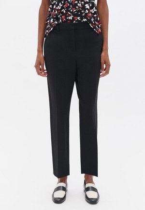 Zwarte op maat gemaakte broek met een gladde textuur, een rechte pijpdesign en riemlussen, gecombineerd met zwart-witte loafers.