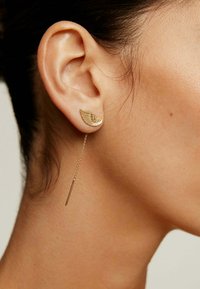 Pendientes de oro con un diseño de alas, con una superficie texturizada y una cadena colgante que se extiende hasta una barra recta en la parte inferior.