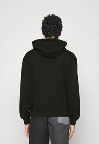 Sudadera con capucha en negro, fabricada en un tejido de textura suave. Presenta hombros caídos y puños y dobladillo acanalados. Diseño simple y sin adornos.