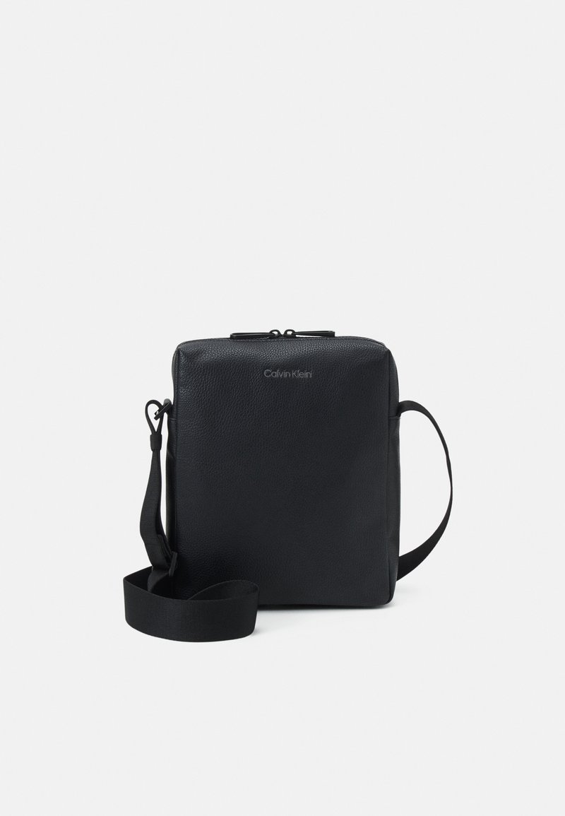 Sac bandoulière rectangulaire noir Calvin Klein avec sangle ajustable et fermeture éclair sur fond blanc.