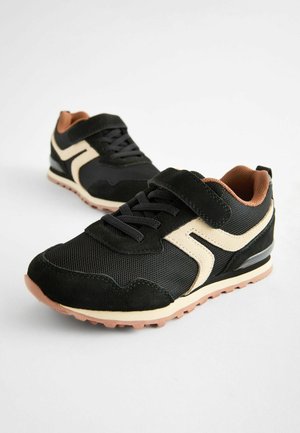 Scarpe sportive nere realizzate con materiali in suede e rete, con un accento color crema, chiusura con lacci e una fascia in Velcro. Suola in gomma.
