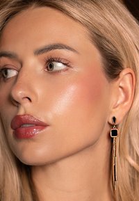 Des boucles d'oreilles pendantes en or et noir présentent un design rectangulaire avec une chaîne fine et des accents carrés, mettant en avant un style contemporain.