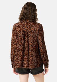 Brun leopardmönstrad blus med långa ärmar, med en plissering bak. Lätt material, avslappnad passform och knäppta manschetter.