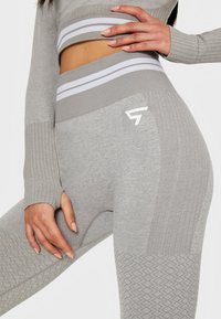 Graue Sportleggings mit strukturierter Musterung, elastischem Taillenbund mit weißen Streifen und einem Logo an der Seite. Weicher Stoff mit gerippten Details.