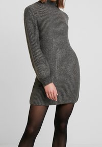 Abito a maglia grigia a coste con maniche lunghe e collo alto, caratterizzato da una silhouette aderente e un tessuto testurizzato.