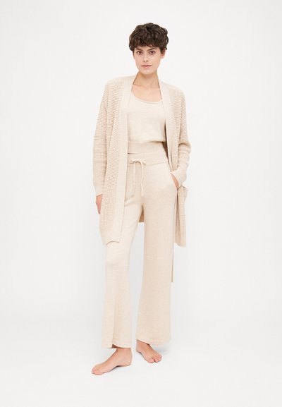Beige knitted cardigan over a matching tank top and wide-leg pants. Soft texture with a loose fit and drawstring waist.