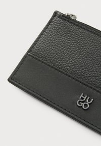 Black leather cardholder with textured surface, smooth accents, visible stitching, and a silver "HUGO" logo on the bottom right.