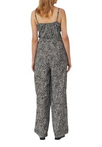 Schwarz-weißer gemusterter Jumpsuit mit cinchierter Taille, weiten Beinen und dünnen Spaghettiträgern, der durchgängig geometrische Designs aufweist.